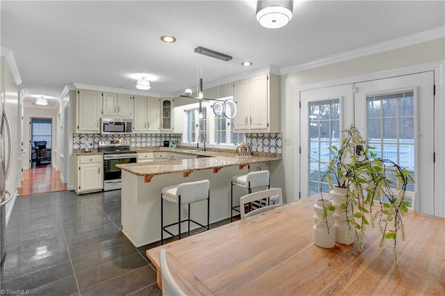 kitchen featuring kitchen peninsula, appliances with stainless steel finishes, backsplash, light stone counters, and ornamental molding