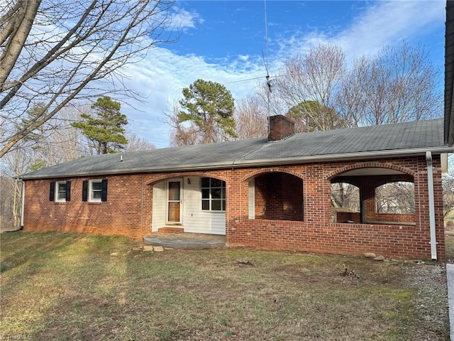 back of house with brick siding, a yard, and a chimney