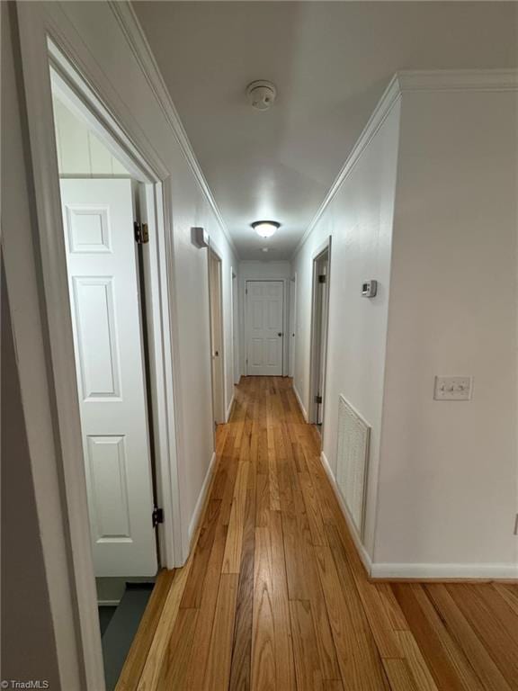 corridor with ornamental molding, visible vents, light wood-style floors, and baseboards