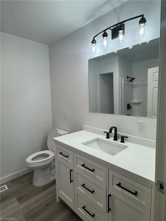 bathroom featuring visible vents, toilet, wood finished floors, walk in shower, and vanity