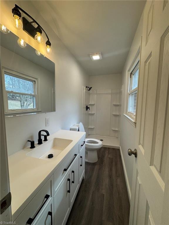 bathroom with a shower, toilet, wood finished floors, vanity, and a healthy amount of sunlight