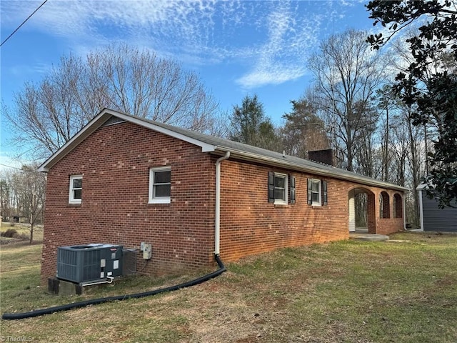 view of property exterior with a yard, brick siding, a chimney, and cooling unit