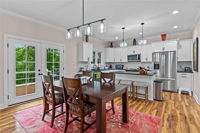 dining space with ornamental molding, light wood-style floors, recessed lighting, and french doors
