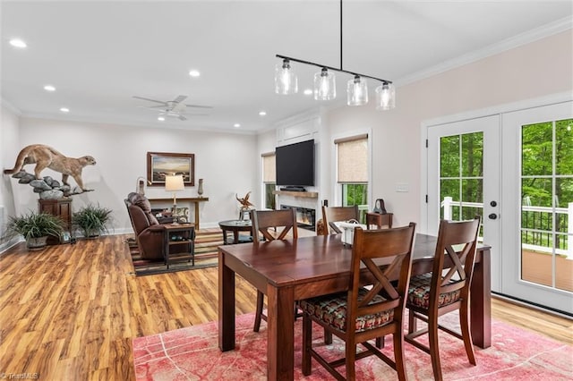dining space featuring crown molding, recessed lighting, light wood-style floors, a glass covered fireplace, and ceiling fan
