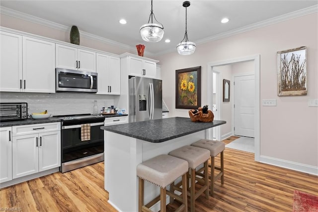 kitchen with appliances with stainless steel finishes, light wood-style flooring, a kitchen breakfast bar, dark countertops, and crown molding