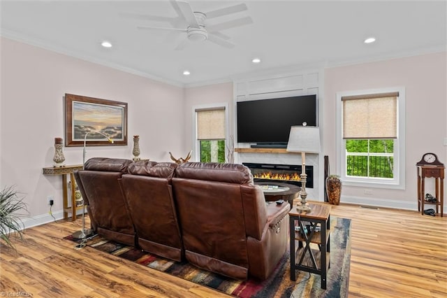 living area with ceiling fan, ornamental molding, healthy amount of natural light, wood finished floors, and recessed lighting