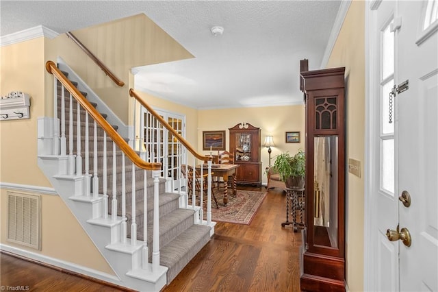 foyer entrance featuring dark wood-type flooring, a textured ceiling, and ornamental molding