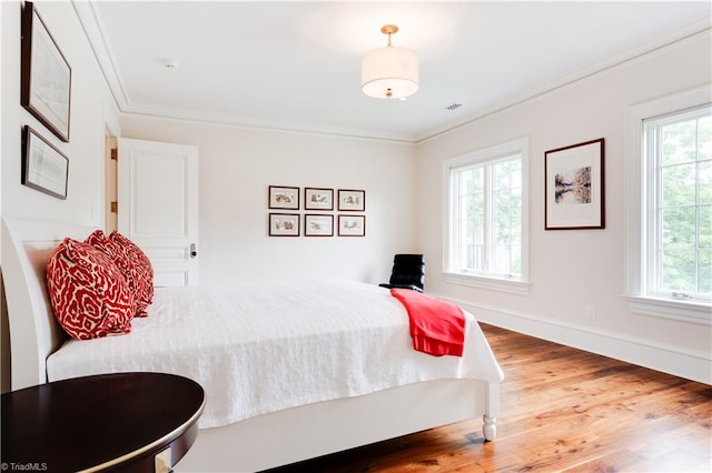 bedroom with ornamental molding, multiple windows, and wood-type flooring