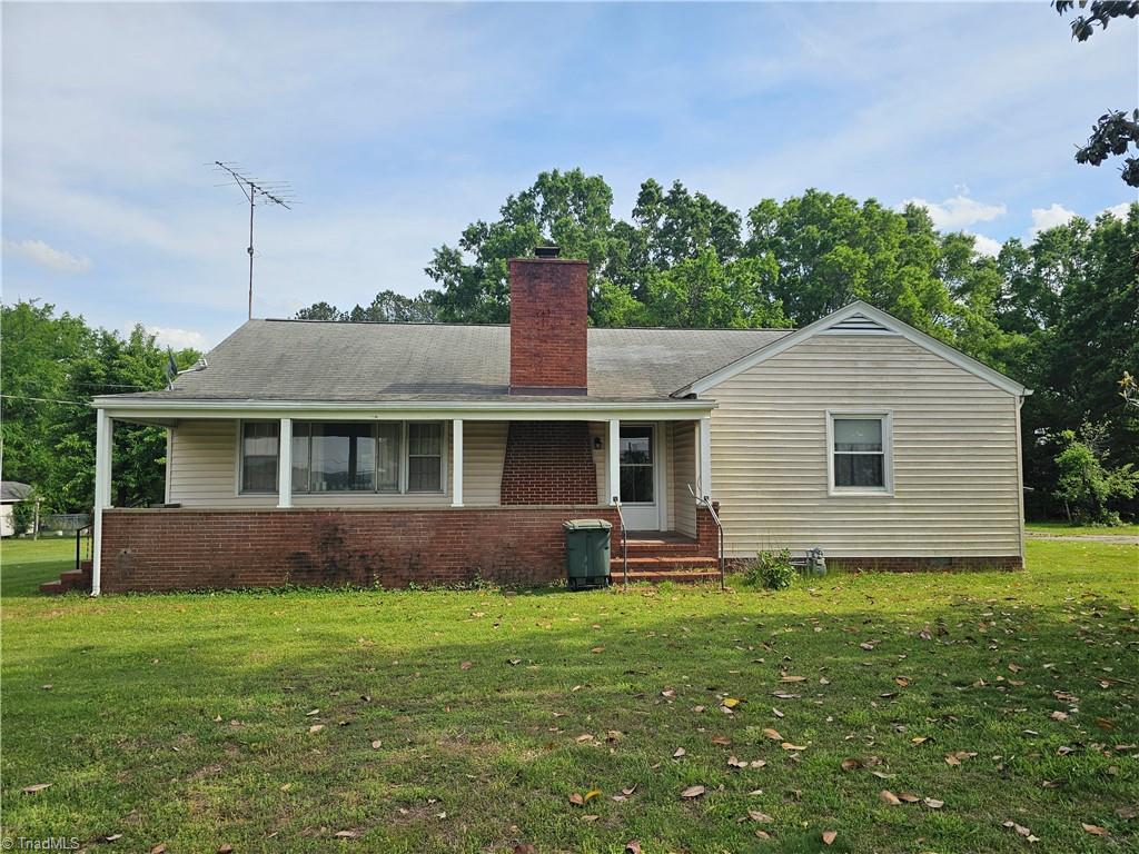 view of front facade with a front yard, a chimney, covered porch, and brick siding