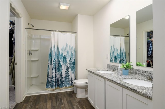 full bath featuring double vanity, a shower stall, a sink, and wood finished floors