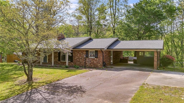 ranch-style house with a chimney, brick siding, an attached carport, driveway, and a front yard