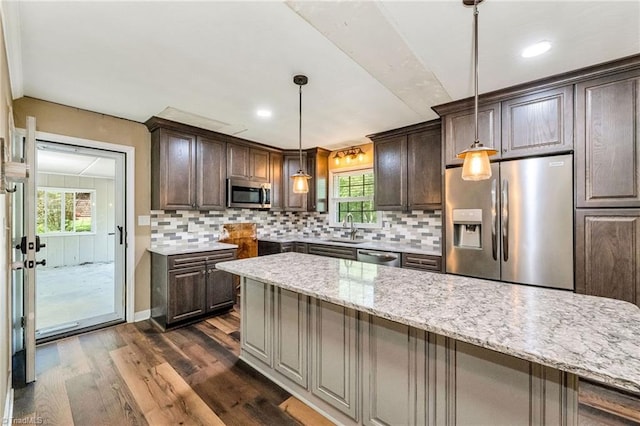 kitchen with a sink, tasteful backsplash, dark wood-type flooring, dark brown cabinetry, and appliances with stainless steel finishes