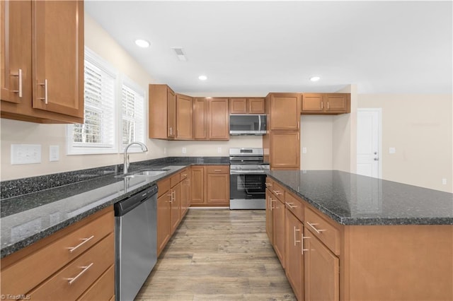 kitchen with light hardwood / wood-style floors, sink, appliances with stainless steel finishes, and dark stone countertops