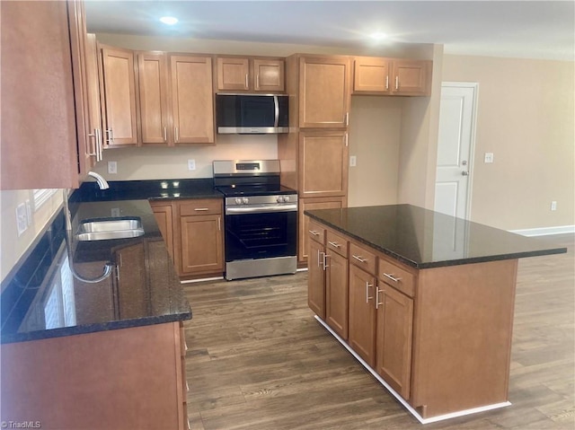 kitchen featuring appliances with stainless steel finishes, a kitchen island, dark hardwood / wood-style flooring, dark stone counters, and sink