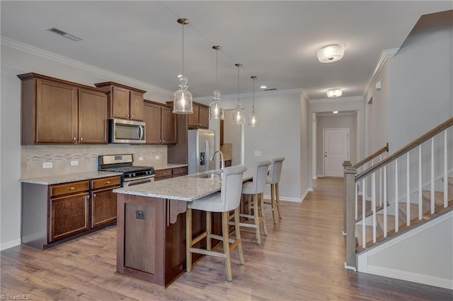 kitchen with an island with sink, stainless steel appliances, hardwood / wood-style floors, a breakfast bar, and light stone counters