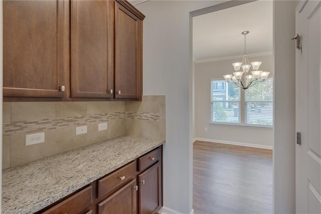 kitchen featuring crown molding, wood-type flooring, tasteful backsplash, light stone counters, and an inviting chandelier