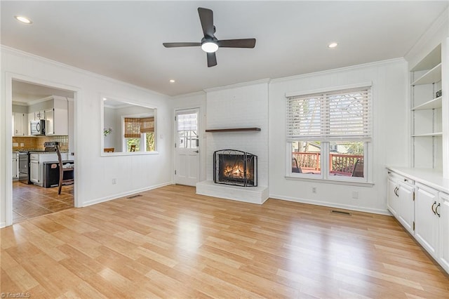 unfurnished living room featuring visible vents, a brick fireplace, ornamental molding, light wood-style flooring, and a ceiling fan