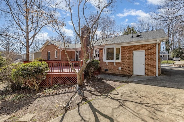 rear view of house featuring driveway, a wooden deck, a chimney, crawl space, and brick siding