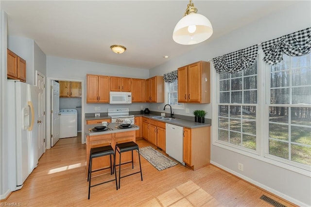 kitchen with washer / dryer, sink, decorative light fixtures, light wood-type flooring, and white appliances