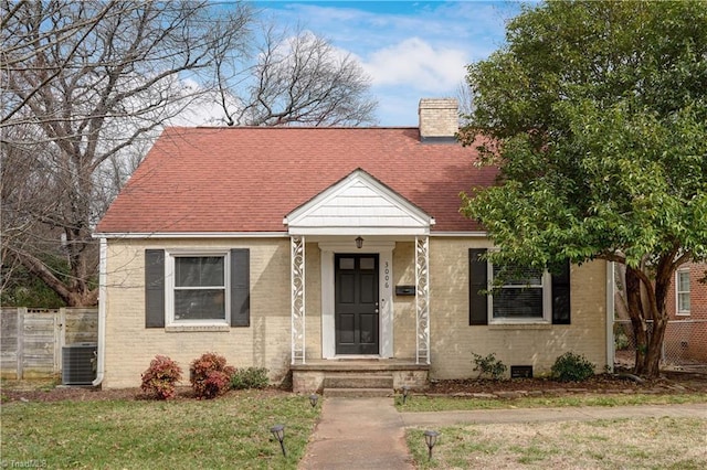 view of front of property featuring a front yard, cooling unit, roof with shingles, a chimney, and brick siding