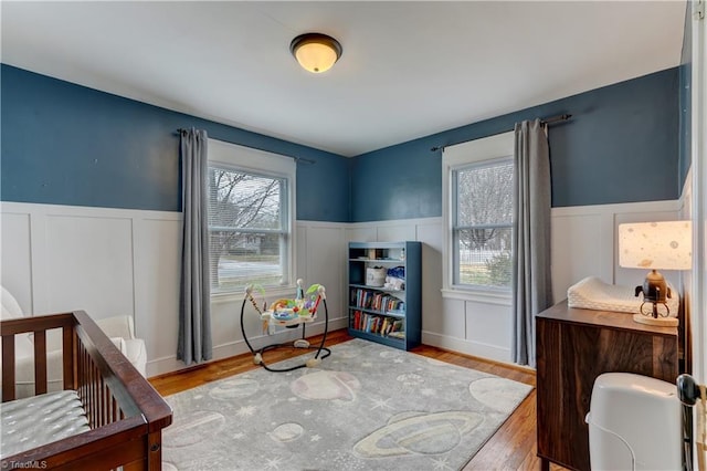 bedroom with multiple windows, wood finished floors, and wainscoting