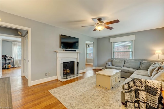 living room featuring light wood finished floors, a fireplace with flush hearth, baseboards, and ceiling fan