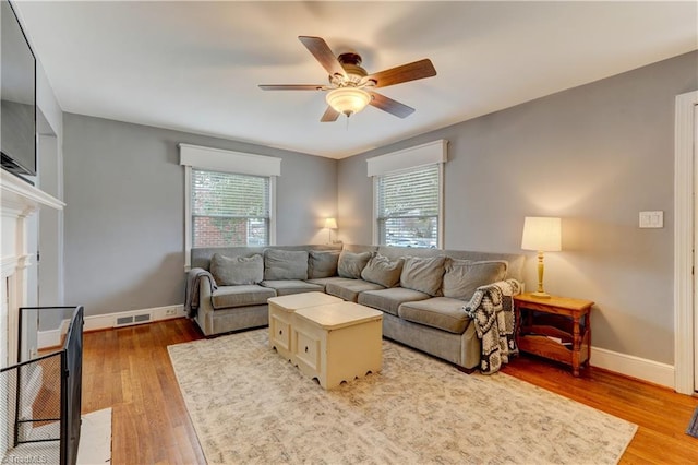 living room featuring baseboards, a healthy amount of sunlight, a ceiling fan, and light wood finished floors