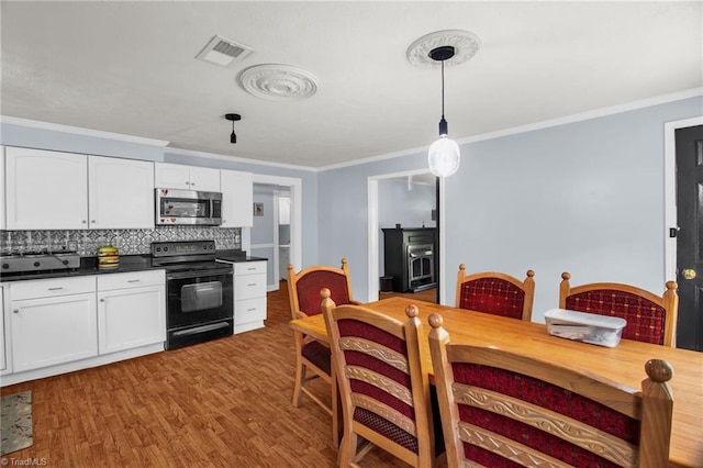 kitchen featuring stainless steel microwave, electric range, dark countertops, crown molding, and white cabinetry