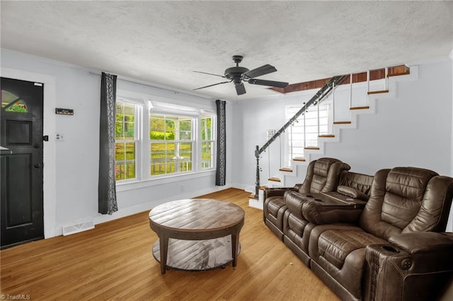living area with baseboards, ceiling fan, light wood-style flooring, a textured ceiling, and stairway