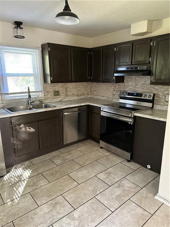 kitchen with appliances with stainless steel finishes, backsplash, a textured ceiling, sink, and pendant lighting