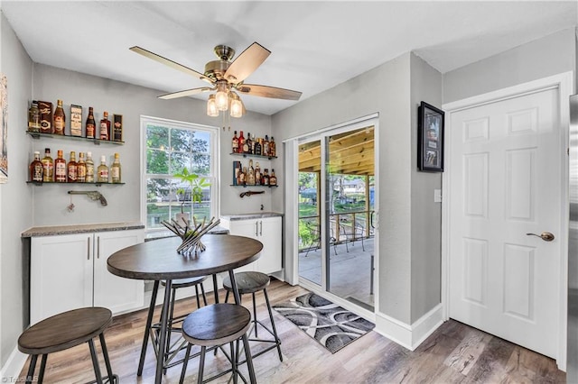 dining space featuring bar, ceiling fan, baseboards, and light wood finished floors
