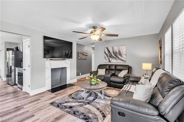 living room featuring baseboards, a fireplace with flush hearth, light wood finished floors, and a ceiling fan