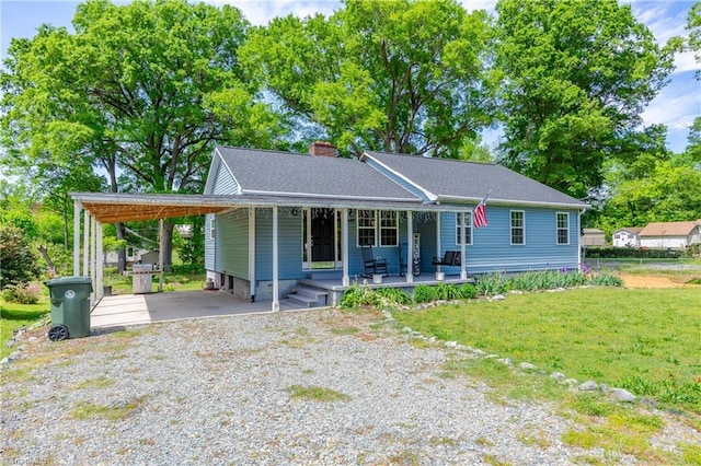 view of front facade with a front lawn, an attached carport, a chimney, covered porch, and gravel driveway