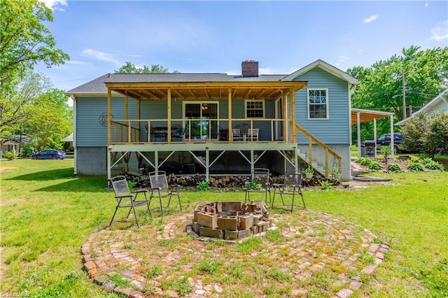 back of house featuring an outdoor fire pit, a wooden deck, stairway, a chimney, and a lawn