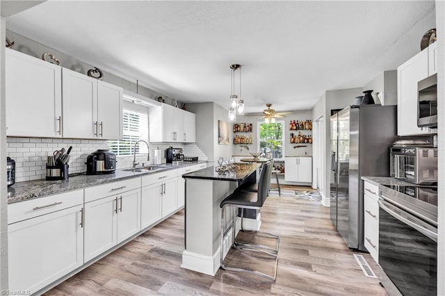 kitchen with a kitchen island, appliances with stainless steel finishes, a sink, white cabinets, and light wood-style flooring