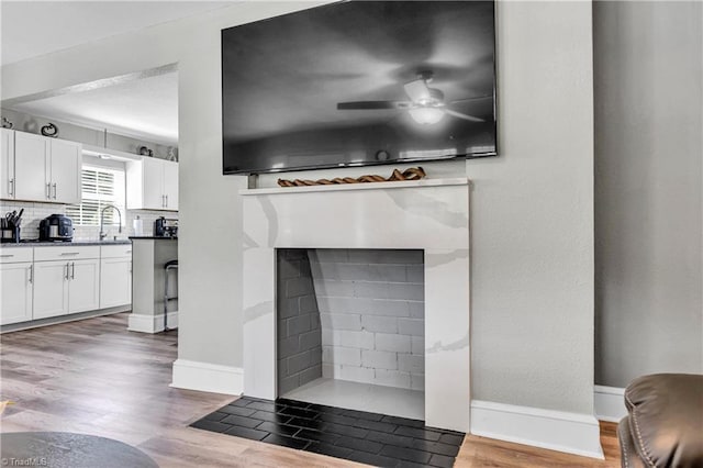 interior details with a fireplace with flush hearth, baseboards, a ceiling fan, and wood finished floors