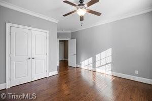 unfurnished bedroom with crown molding, dark wood-type flooring, a closet, and ceiling fan