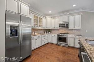 kitchen with tasteful backsplash, ornamental molding, appliances with stainless steel finishes, light stone countertops, and white cabinets