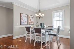 dining area featuring dark wood-type flooring, ornamental molding, a chandelier, and a healthy amount of sunlight