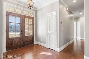 foyer entrance featuring a notable chandelier, crown molding, dark wood-type flooring, and french doors