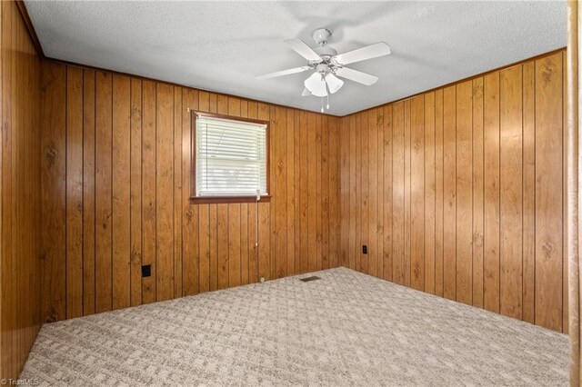 carpeted empty room with ceiling fan, wood walls, and a textured ceiling