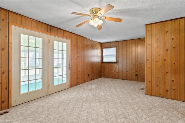 carpeted spare room with ceiling fan, wood walls, and a textured ceiling