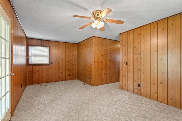 carpeted empty room featuring a textured ceiling, wood walls, and ceiling fan