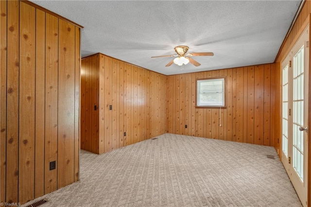 carpeted empty room featuring ceiling fan, wooden walls, and a textured ceiling