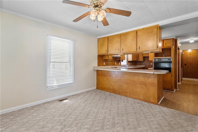 kitchen featuring light colored carpet, kitchen peninsula, oven, and ornamental molding