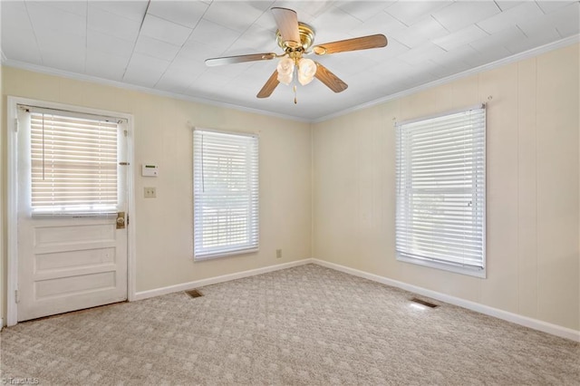 carpeted spare room featuring ornamental molding, ceiling fan, and a healthy amount of sunlight