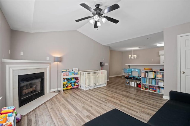 game room featuring vaulted ceiling, wood finished floors, a tile fireplace, baseboards, and ceiling fan with notable chandelier
