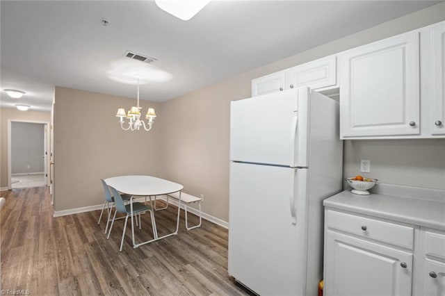 kitchen with visible vents, freestanding refrigerator, an inviting chandelier, wood finished floors, and white cabinetry