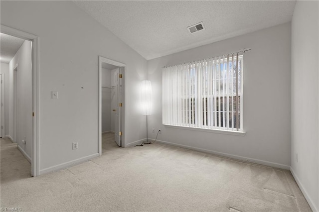 unfurnished bedroom with light carpet, a walk in closet, vaulted ceiling, a textured ceiling, and a closet