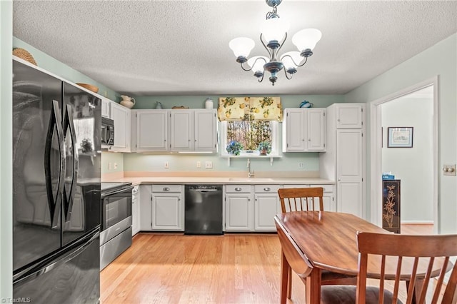 kitchen with a chandelier, black appliances, light countertops, and light wood-style floors